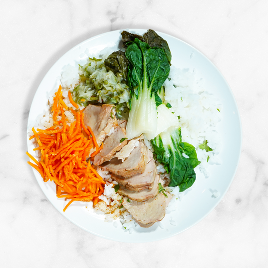 Plate of rice with sliced meat, carrots, and greens on a marble surface
