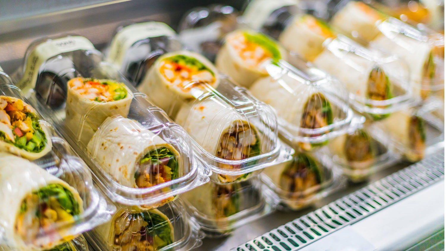 Pre-packaged wraps with vegetables in clear plastic containers on a metal tray.