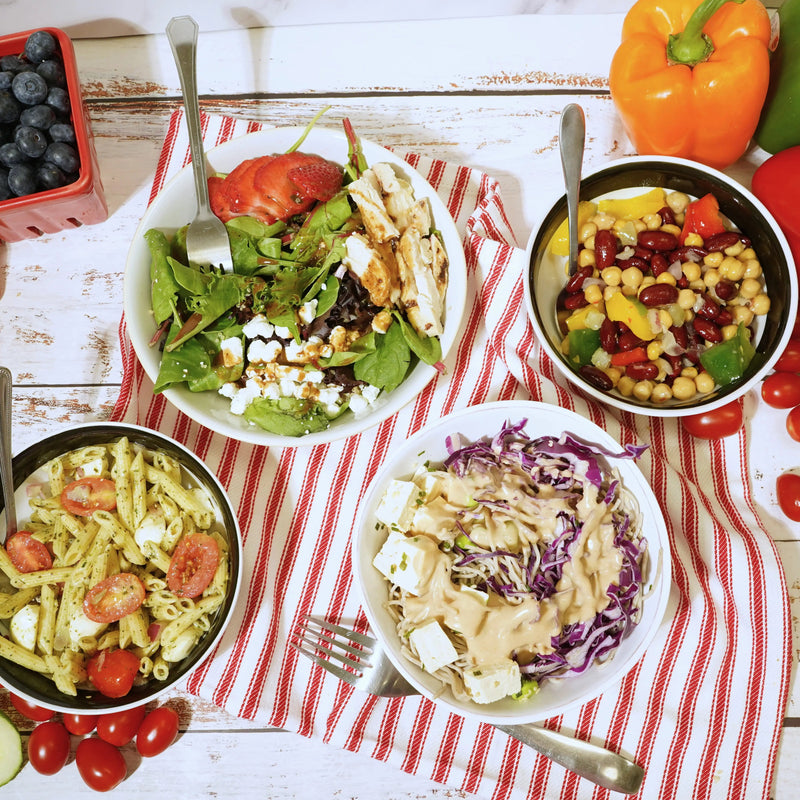 Assorted salads with pasta and vegetables on a red and white striped tablecloth.