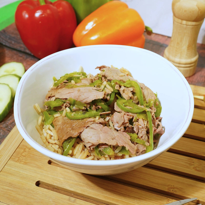 Bowl of stir-fried vegetables and meat on a wooden cutting board with bell peppers in the background.
