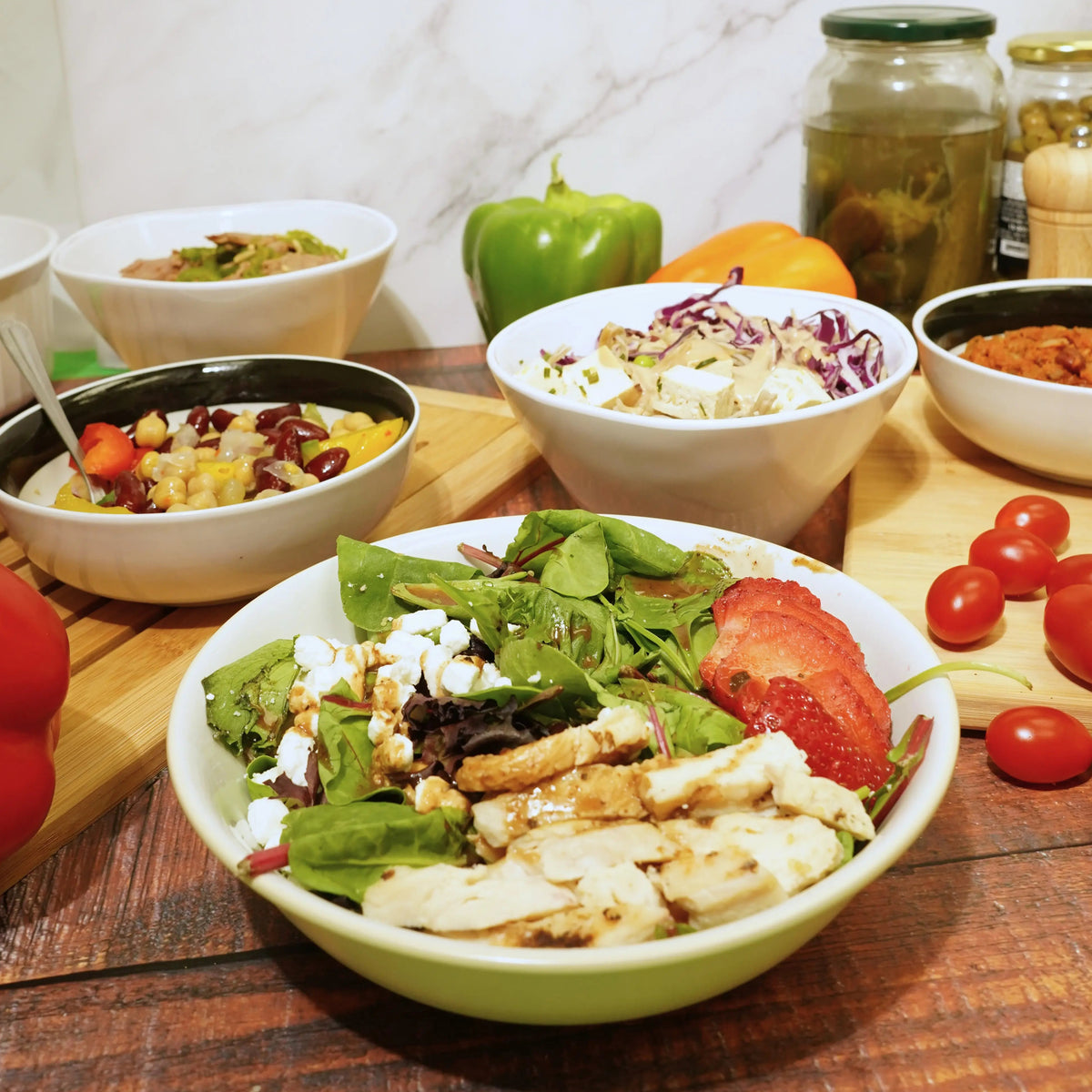 Assorted salads and ingredients on a wooden table with a marble wall background